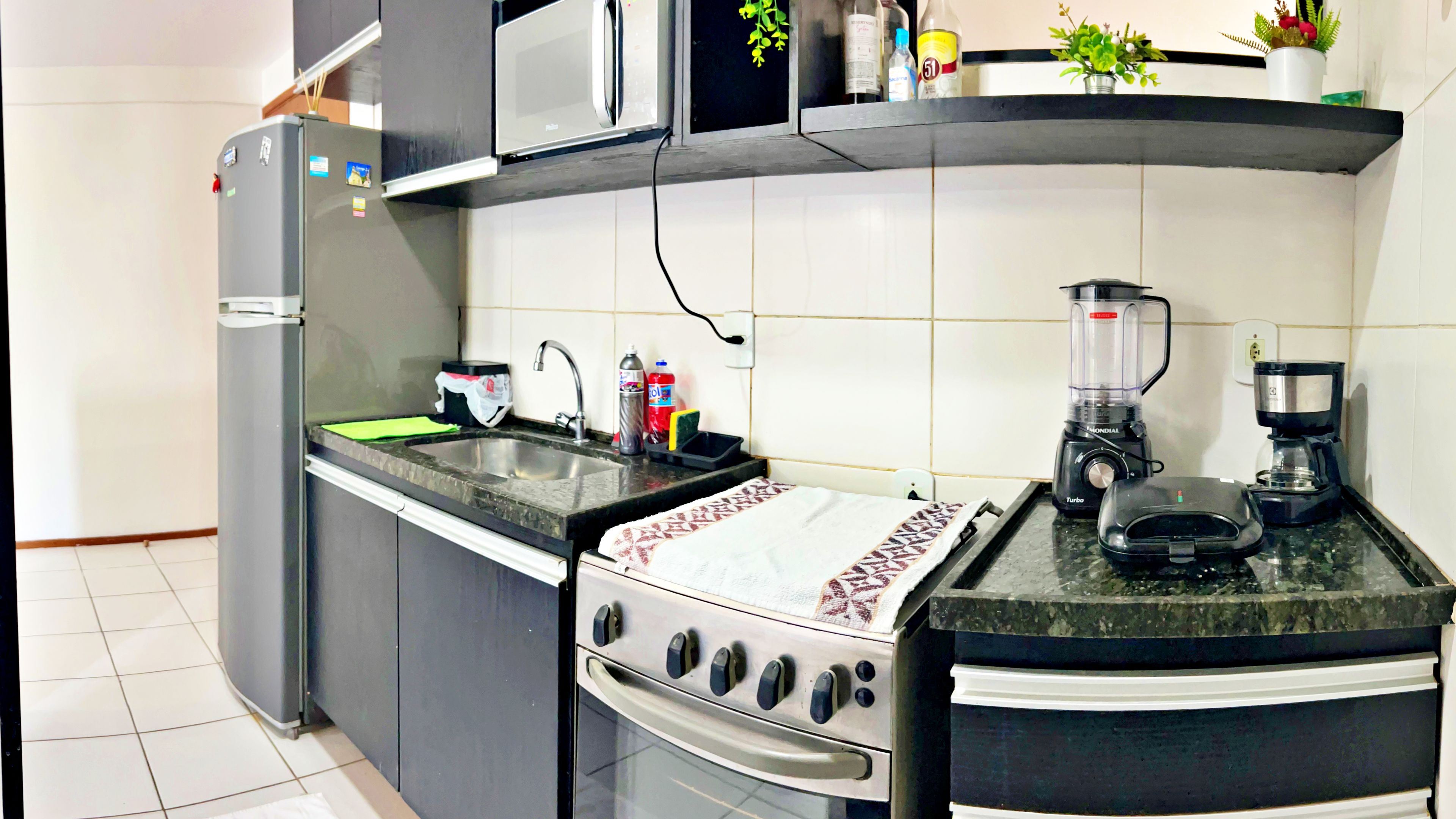 Eine kompakte Küche mit Kühlschrank, Mikrowelle, Herd, Spüle und Kaffeemaschine.