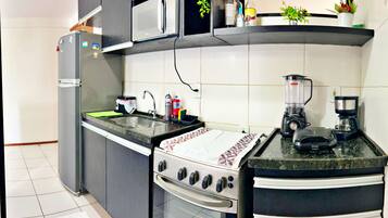 Eine kompakte Küche mit Kühlschrank, Mikrowelle, Herd, Spüle und Kaffeemaschine.