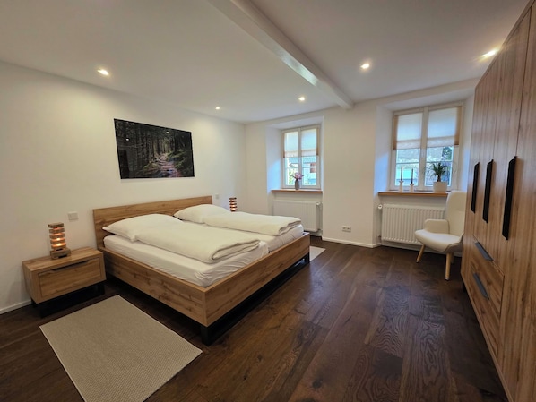Un dormitorio moderno con una cama de madera, una mesita de noche, un radiador y una ventana con persianas.