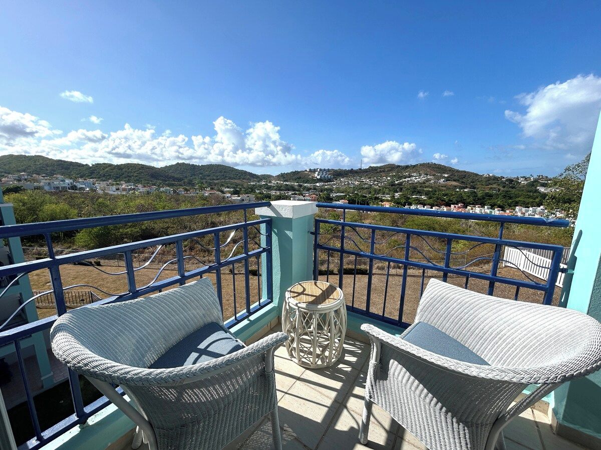 A balcony with wicker furniture and a view of a hilly landscape.