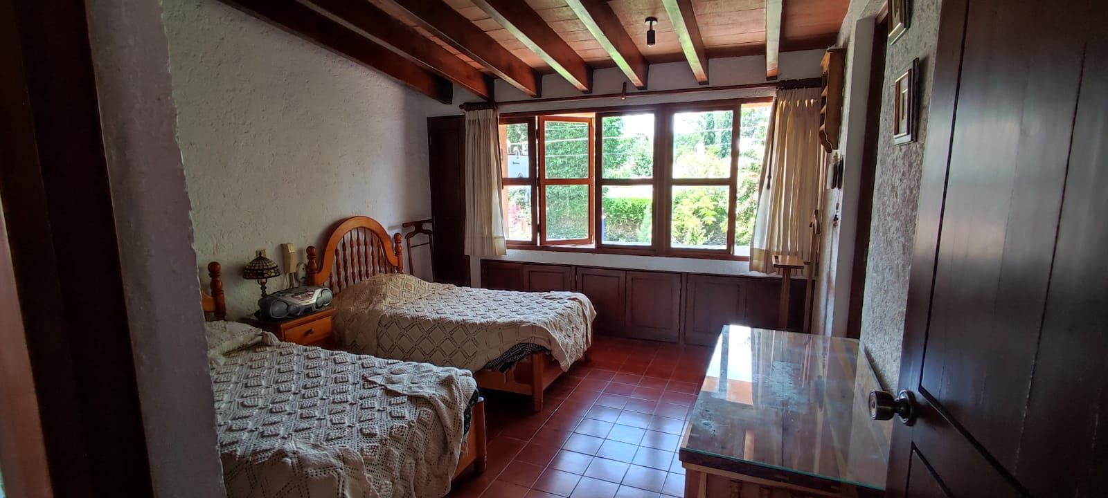 Une chambre avec deux lits, une table en bois et une fenêtre avec des rideaux.