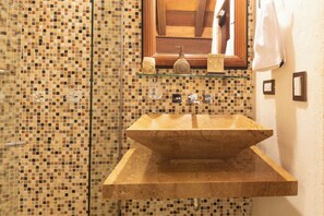 A bathroom with a mosaic tile wall, a wooden vanity with a sink, and a glass shelf with decorative items. - La Muralla Rooftop Duplex Jacuzzi & View (Cartagena de Indias)