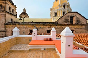 A rooftop terrace with a tiled floor, a cushioned seating area, and a view of historical buildings. - La Muralla Rooftop Duplex Jacuzzi & View (Cartagena de Indias)