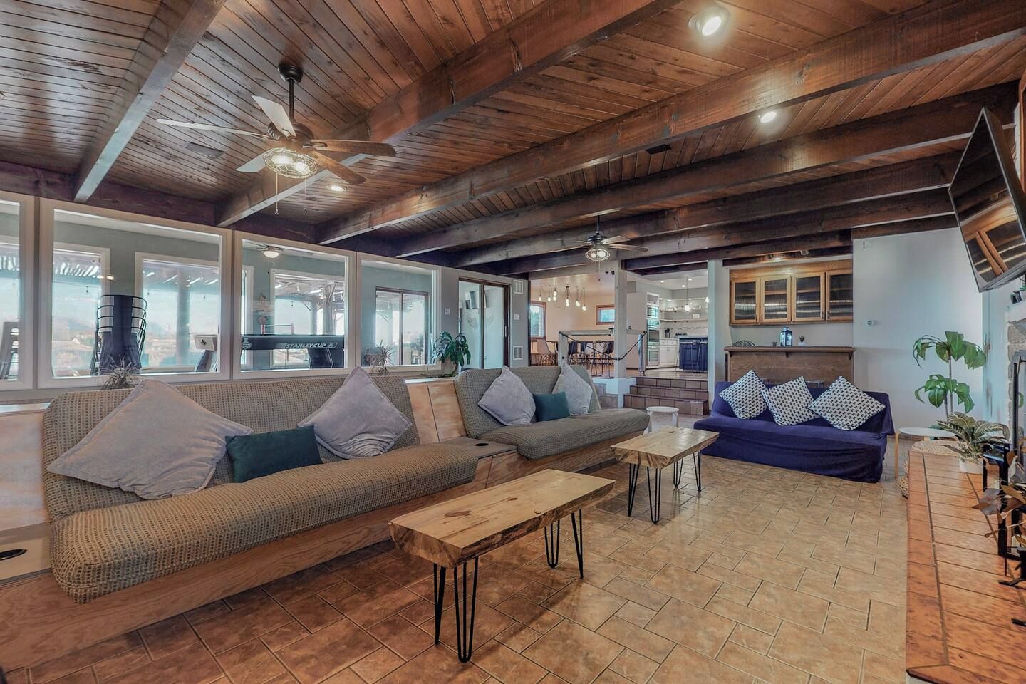 A spacious living area with a high ceiling, wooden beams, and large windows.