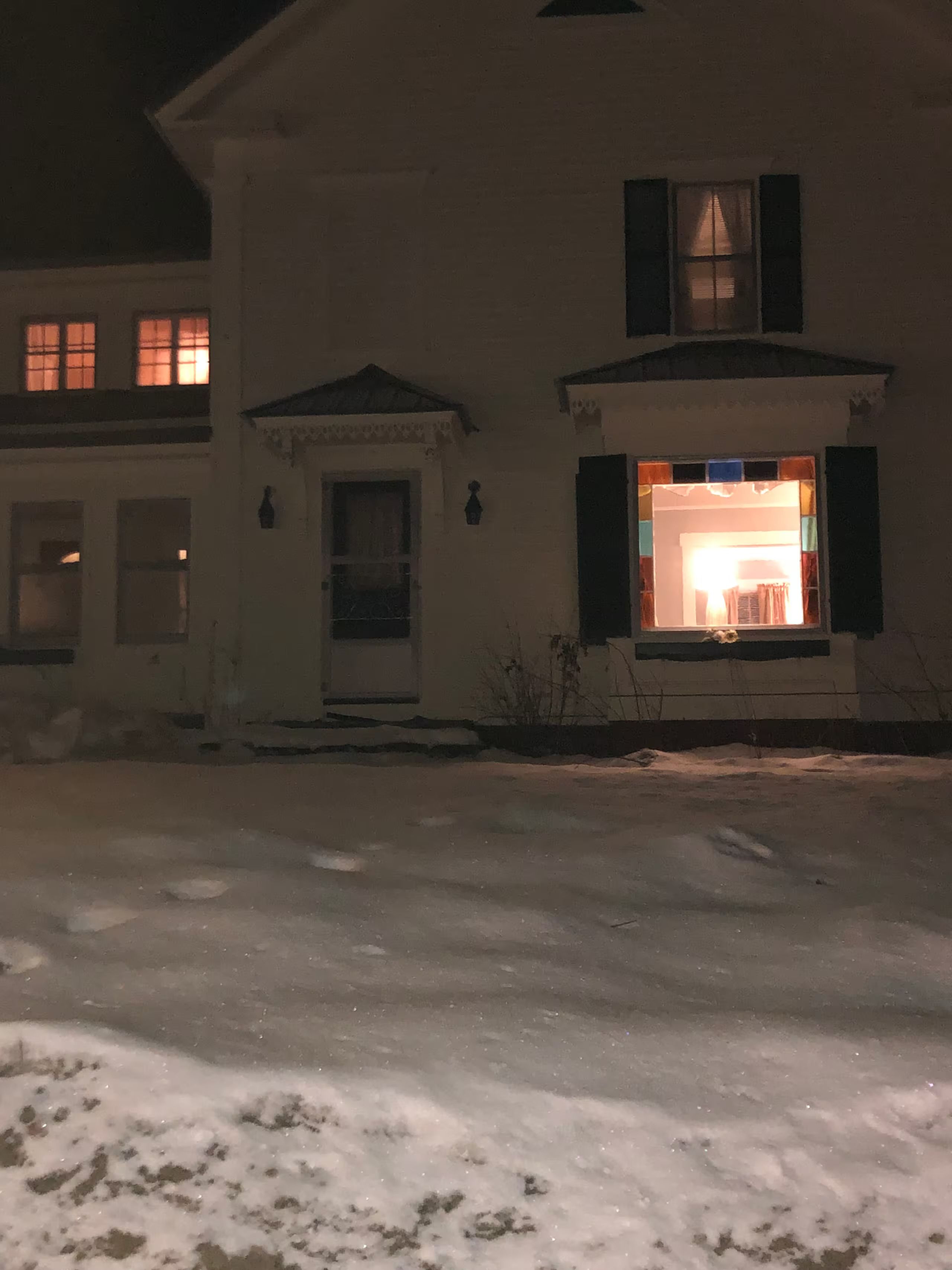 A two-story building with a front door and windows, a driveway, and a snow-covered ground.