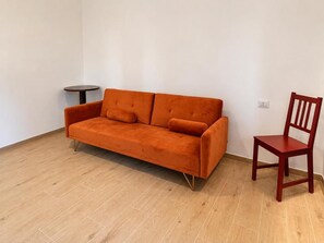 A room with a sofa and a chair, a small table, and a light switch on the wall.