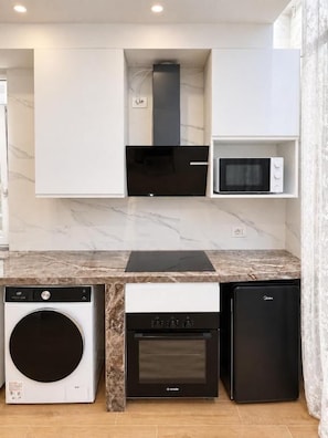 A compact kitchen with a washing machine, oven, microwave, and a built-in range hood.