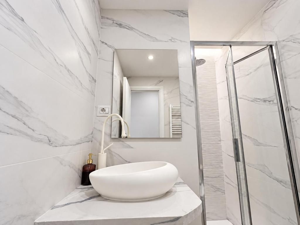 Un bagno con un lavandino bianco, uno specchio e uno spazio doccia.
