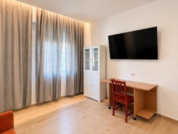 A room with a wooden desk, a television mounted on the wall, and a cabinet.