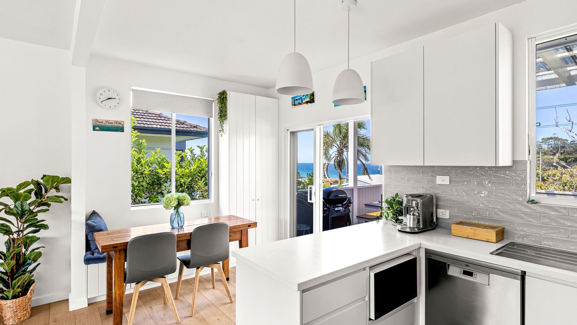 A modern kitchen with a white countertop, a built-in dishwasher, and a view of the ocean through large windows.