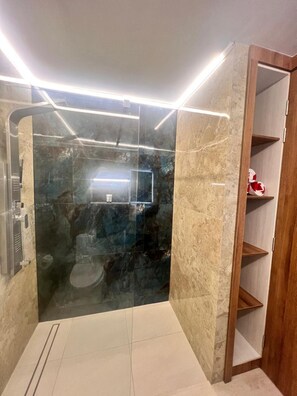Une salle de bain moderne dotée d’une douche à parois de verre, de murs en marbre et d’un meuble-lavabo en bois avec des étagères ouvertes.