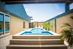 Une piscine extérieure moderne, accessible par des marches, entourée de murs et agrémentée de plantes en pot.