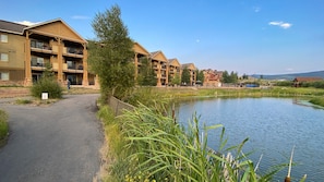 A multi-story building with balconies, a paved walkway, and a body of water. - WorldMark Rocky Mountain Preserve - 2BR Twin Suite with Fireplace at 8,000 Ft (Granby)