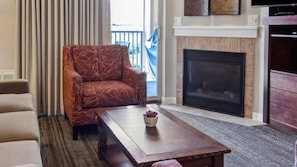 A living room with a red patterned armchair, a wooden coffee table with a plant, a fireplace, and a television on a wooden stand. - WorldMark Rocky Mountain Preserve - 2BR Twin Suite with Fireplace at 8,000 Ft (Granby)