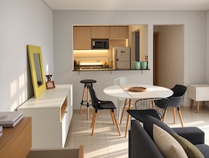 Una cocina moderna con microondas, refrigerador y gabinetes de madera. Hay un comedor con mesa blanca y sillas negras.