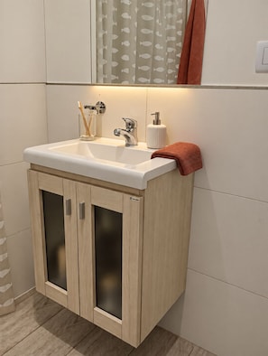 Un baño con un lavamanos blanco, armarios de madera y un espejo arriba.