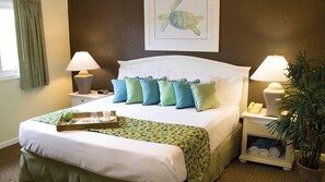 Una cama bien tendida con una bandeja de alimentos para el desayuno, un arreglo de almohadas y un cuadro de una tortuga en la pared.