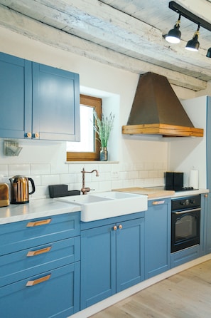 A kitchen with blue cabinets, a white sink, and a wooden range hood. - Charming stonehouse Ramiro (Podašpilje)