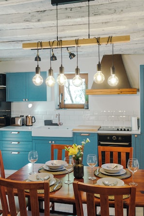 A kitchen with teal cabinets, a wooden dining table set for four, and a hanging light fixture above. - Charming stonehouse Ramiro (Podašpilje)