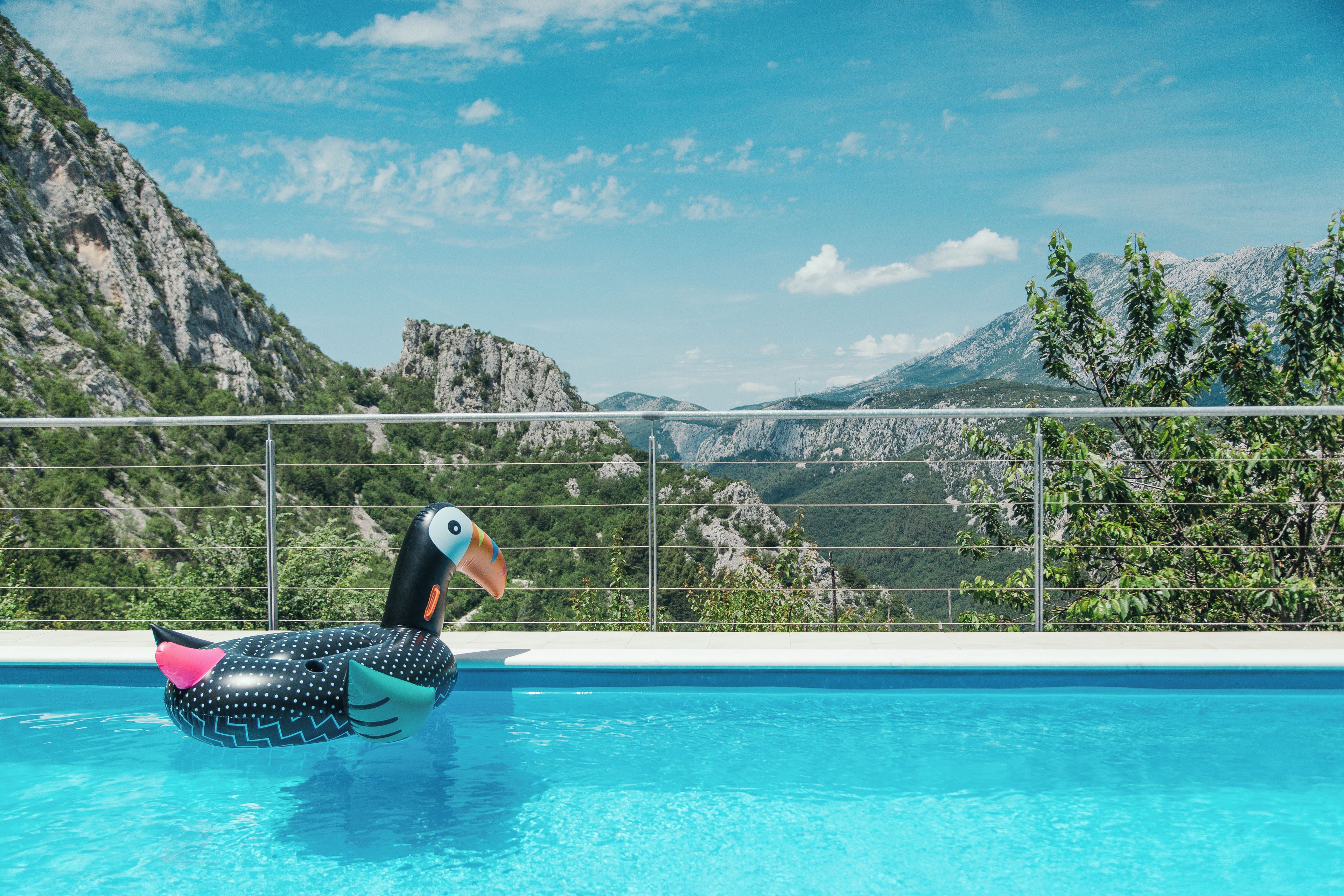 A pool with a polka-dotted inflatable duck, surrounded by a metal railing, with a mountainous landscape in the background.