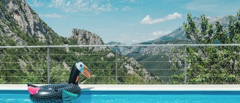 A pool with a polka-dotted inflatable duck, surrounded by a metal railing, with a mountainous landscape in the background.