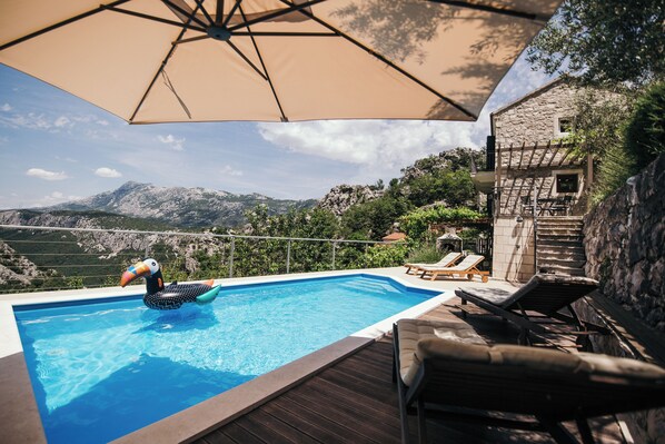 A swimming pool with a view of mountains, a wooden deck, and lounge chairs. - Charming stonehouse Ramiro (Podašpilje)