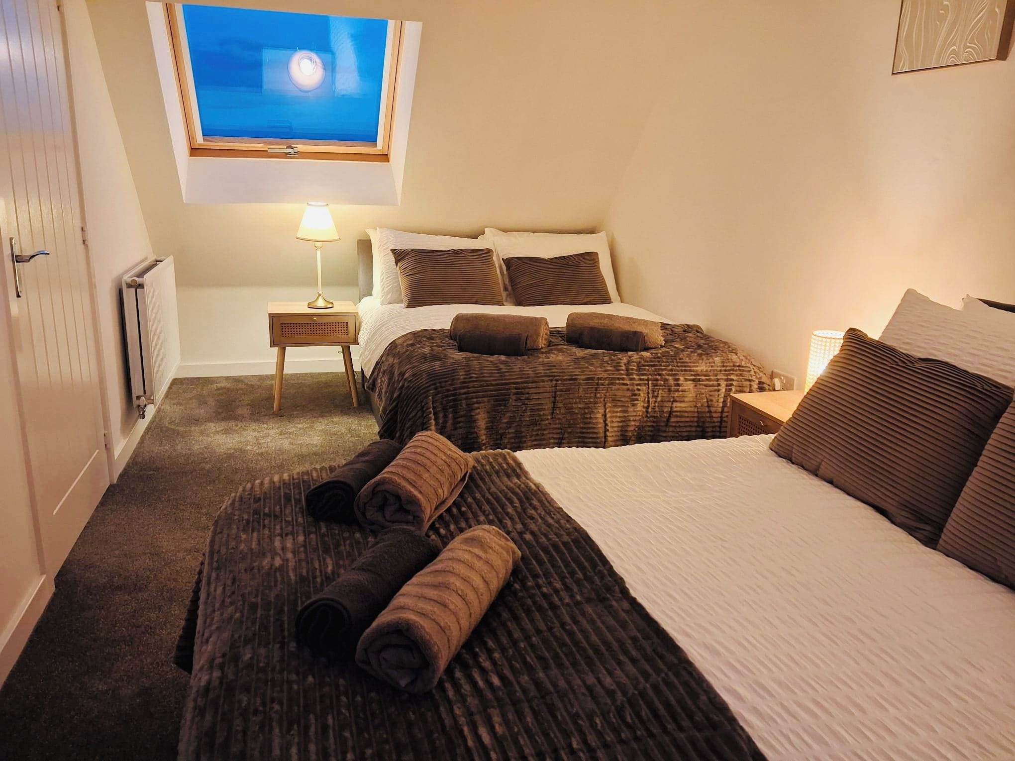 Een slaapkamer met twee bedden, een raam met uitzicht, een nachtkastje met een lamp en een radiator.