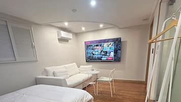 A modern bedroom with a bed, a sofa, a TV mounted on the wall, and a wooden floor.