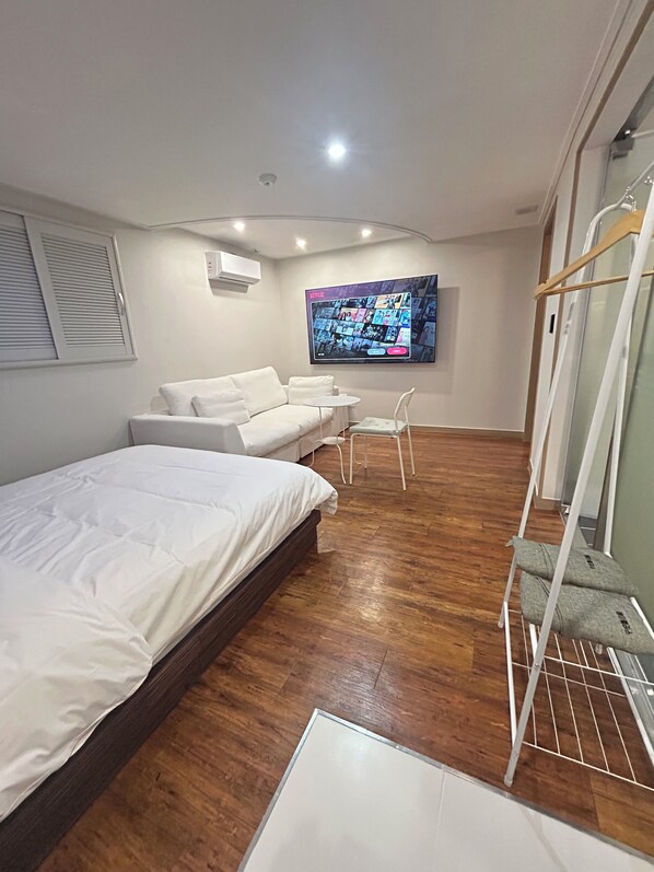 Un dormitorio moderno con cama, sofá, televisor montado en la pared y suelo de madera.