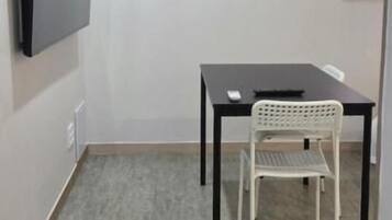 A room with a flat-screen TV mounted on the wall, a table with a chair, and an air conditioning unit.