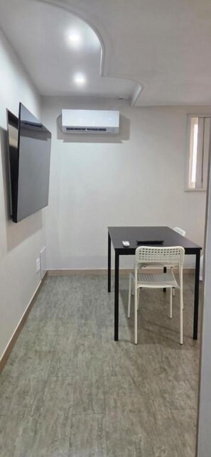 Habitación con televisión de pantalla plana montada en la pared, una mesa con una silla y un equipo de aire acondicionado.