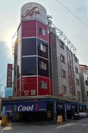Un edificio de varios pisos con una fachada llamativa roja y blanca, un letrero con caracteres coreanos y un escaparate con un rótulo que dice 'Cool'.
