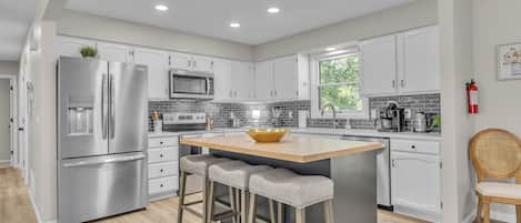 A modern kitchen with stainless steel appliances, a central island with stools, and a view of the outdoors.