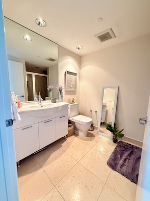 Un baño moderno con tocador blanco, inodoro, espejo grande y alfombra morada.