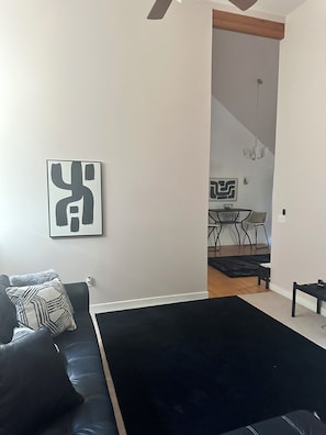 Un saló modern amb un sofà negre, una catifa negra i una zona de menjador al fons.