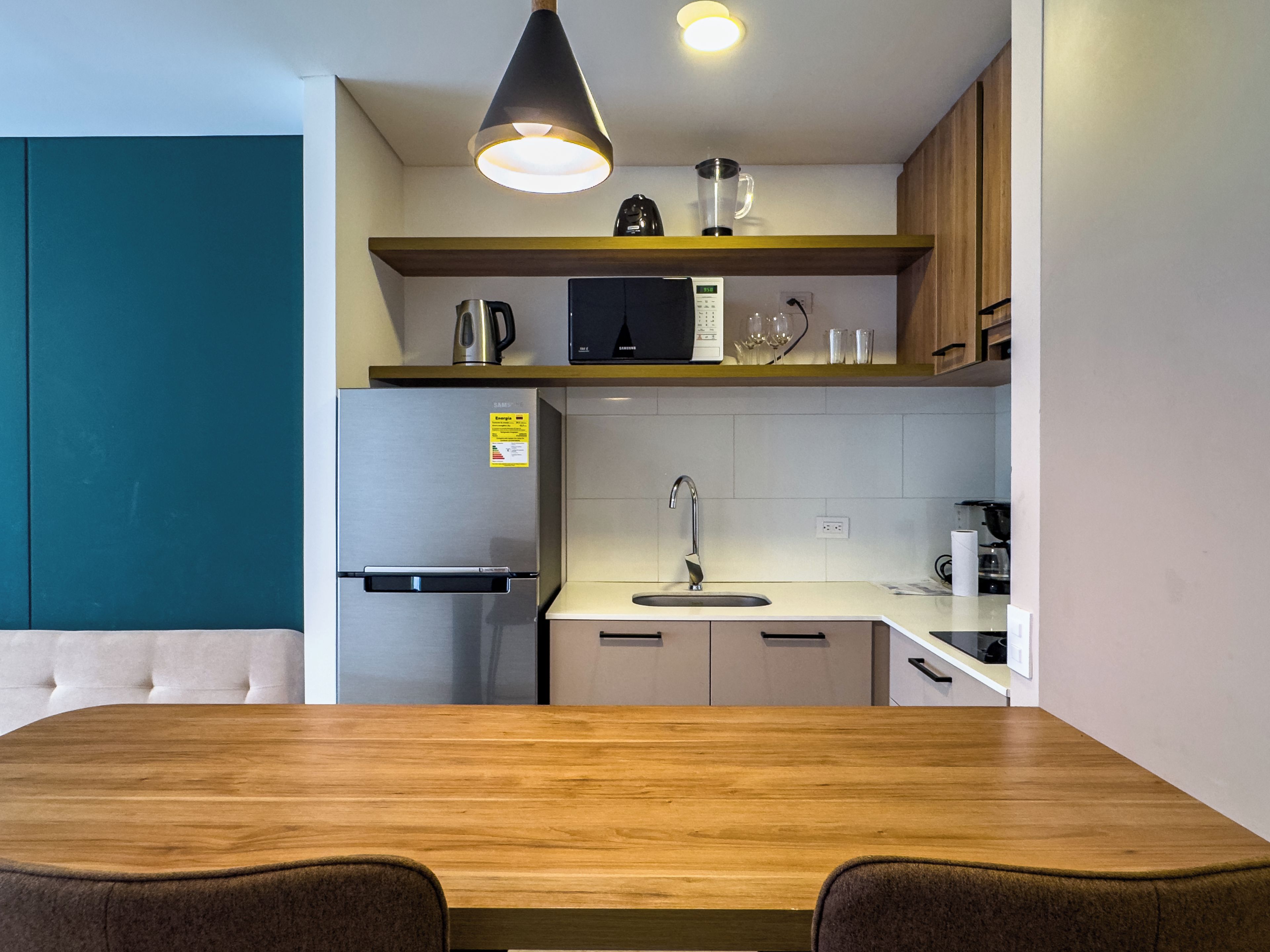 Una cocina moderna con una mesa de comedor de madera, electrodomésticos de acero inoxidable y una pared de acento color verde azulado.