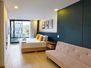 A modern hotel room with a large bed, a sofa, a desk, and a view of the city through a large window. - Amazing Loft in Usaquen (Bogotá)