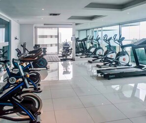 Une salle de sport équipée de matériel d’exercice, notamment des tapis de course et des vélos d’appartement, et dotée d’une grande fenêtre offrant une vue sur la ville.