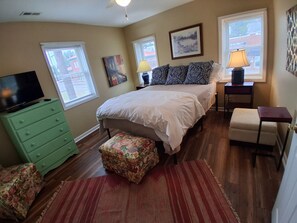 Une chambre à coucher avec un lit, une commode verte, un téléviseur et une fenêtre avec des stores.