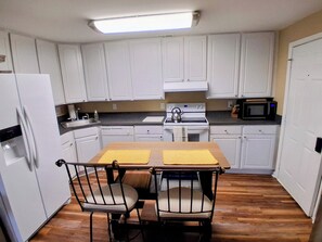 Una cucina compatta con mobili bianchi, un frigorifero, un fornello, un forno a microonde e un tavolo da pranzo con due sedie.