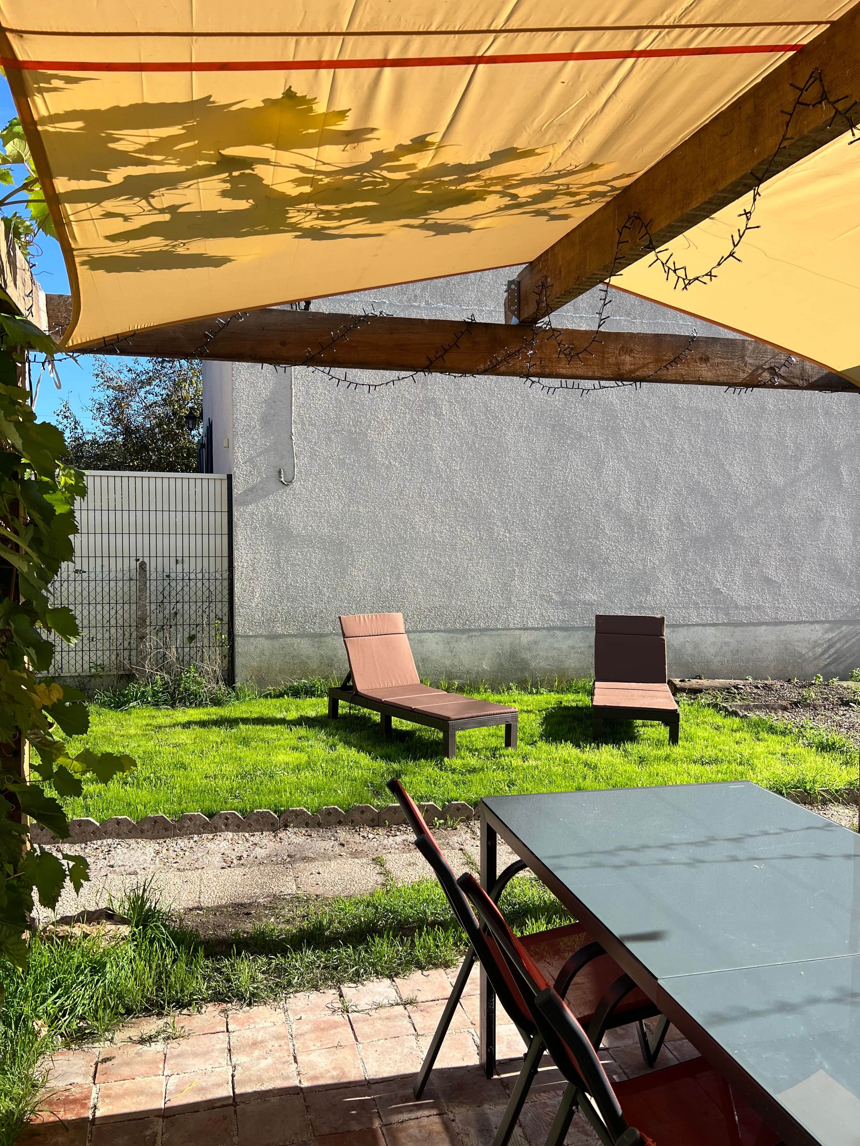 Un espace patio comprenant deux chaises longues, une table et une structure de protection solaire jaune.
