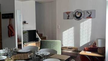 Un coin repas avec une table dressée pour quatre personnes, des chaises, un canapé et un téléviseur en arrière-plan.