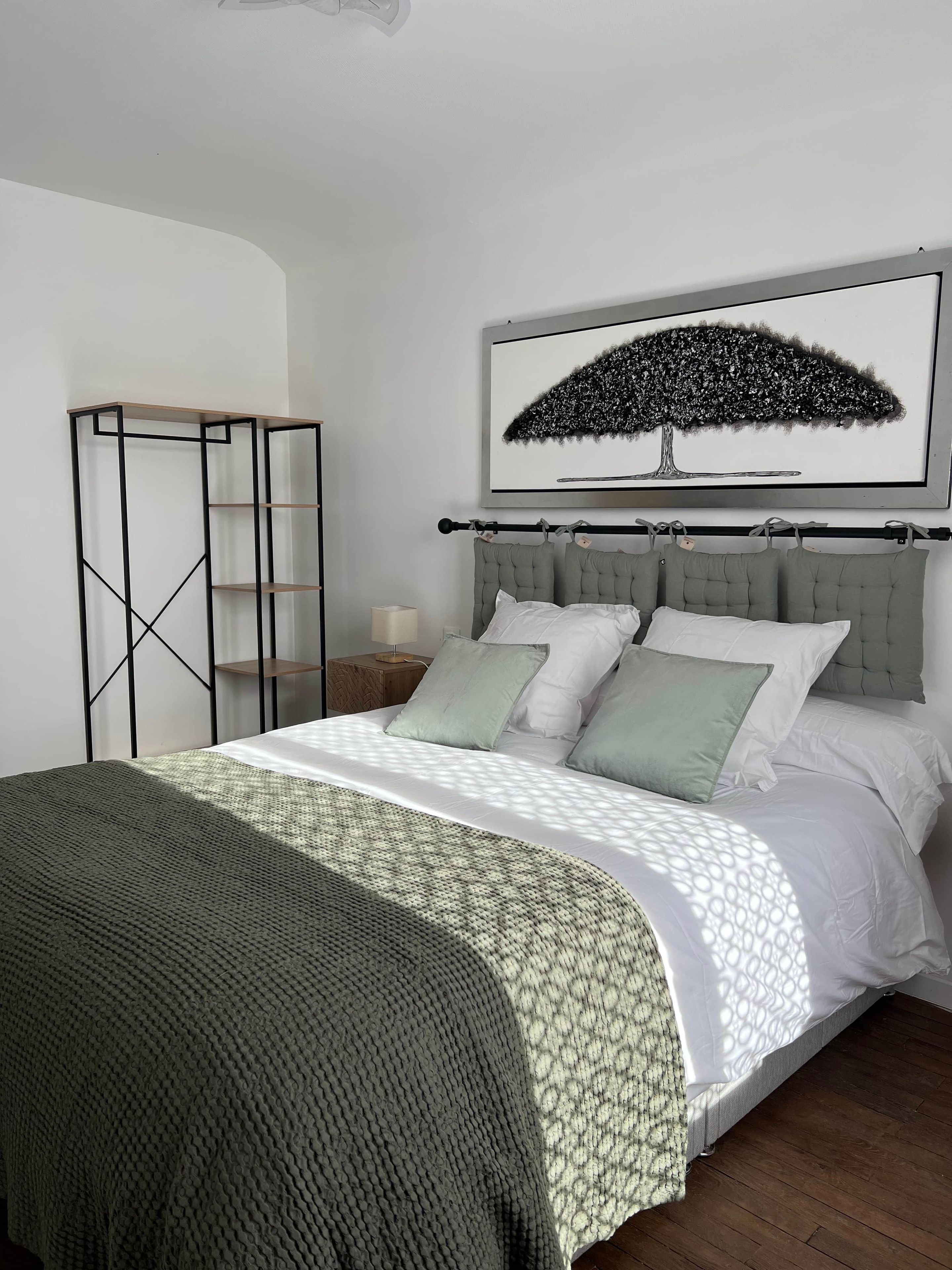 A bedroom with a bed, a headboard, a nightstand, a lamp, a framed picture, and a wardrobe.