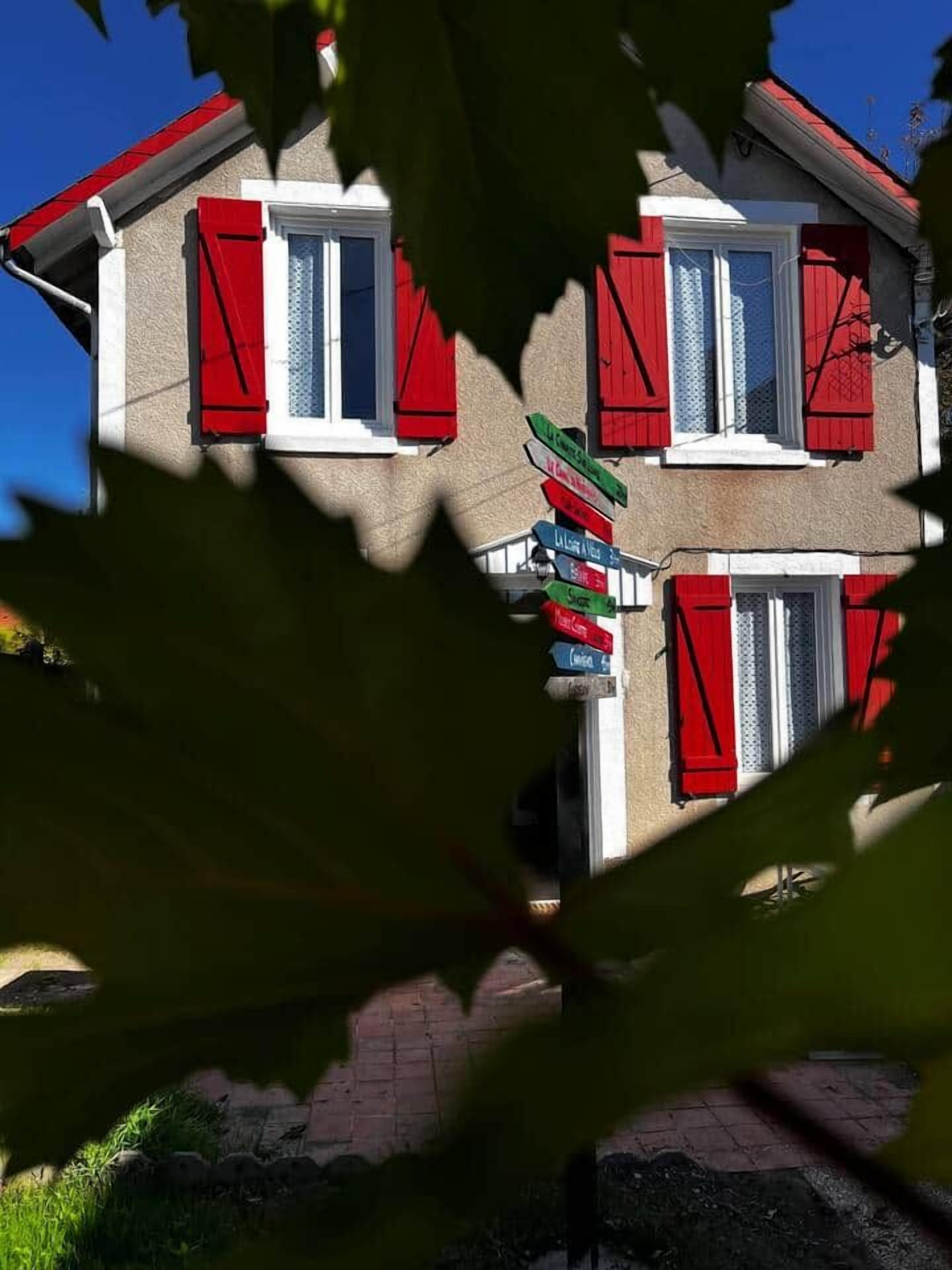 Un bâtiment à deux étages, doté de volets rouges et d’un panneau indicateur comportant plusieurs panneaux directionnels.