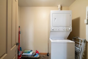 Una sala de bugaderia amb una rentadora i una assecadora apilades, una fregona, productes de neteja i un radiador.