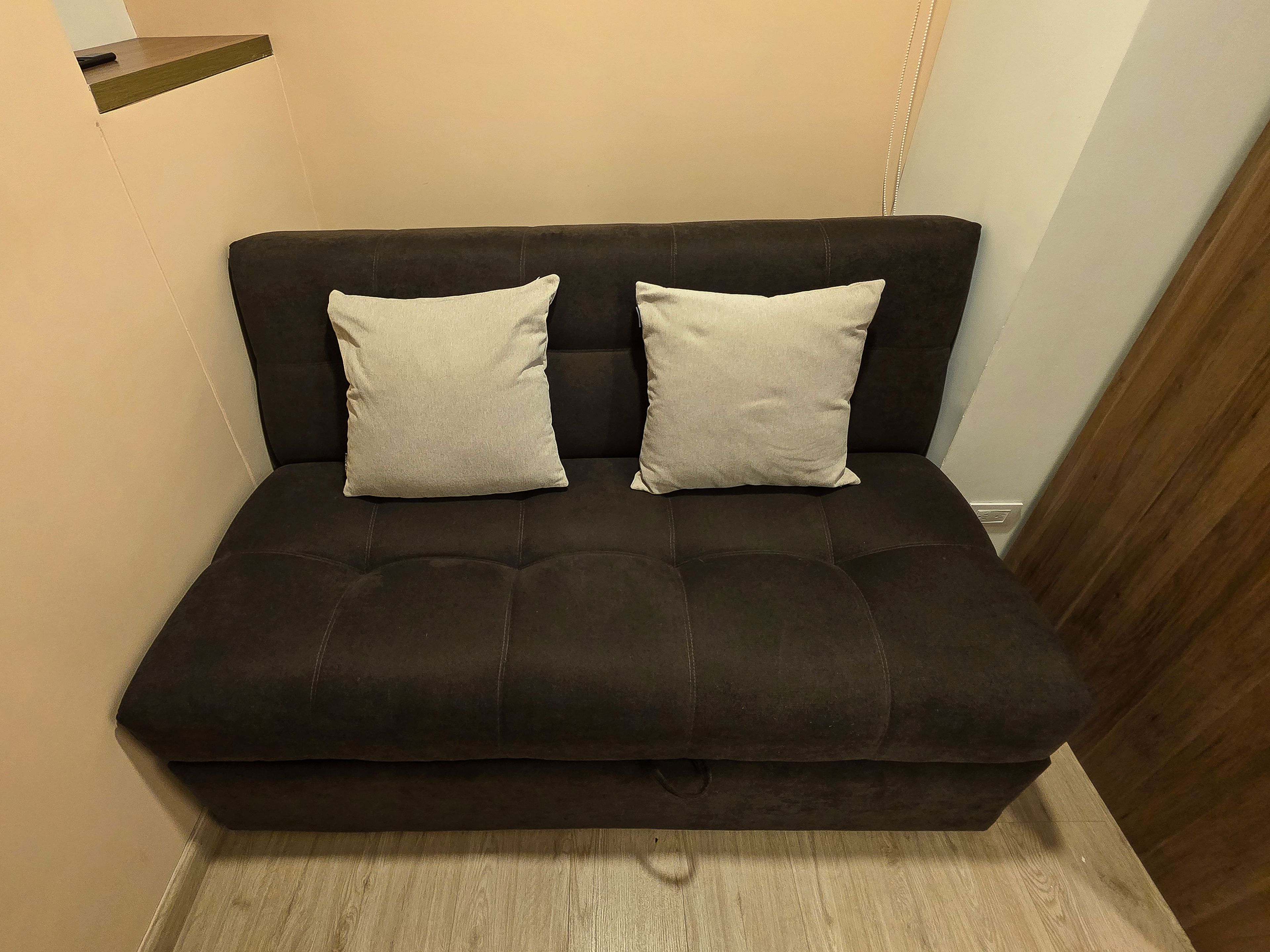 Un sofá de color oscuro con dos almohadas y piso de madera.
