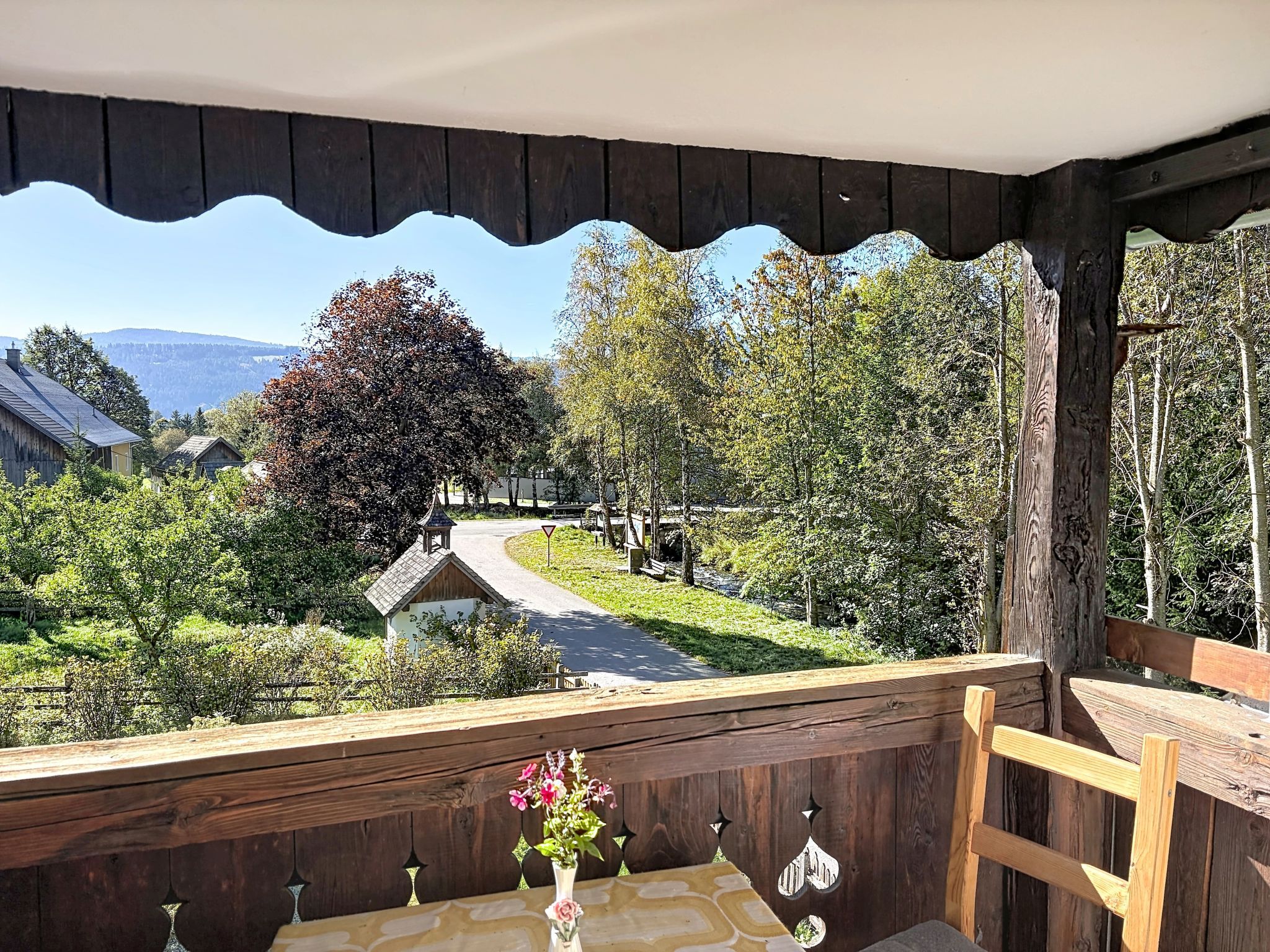 Un balcon en bois offrant une vue sur une route sinueuse, des arbres et un petit bâtiment.