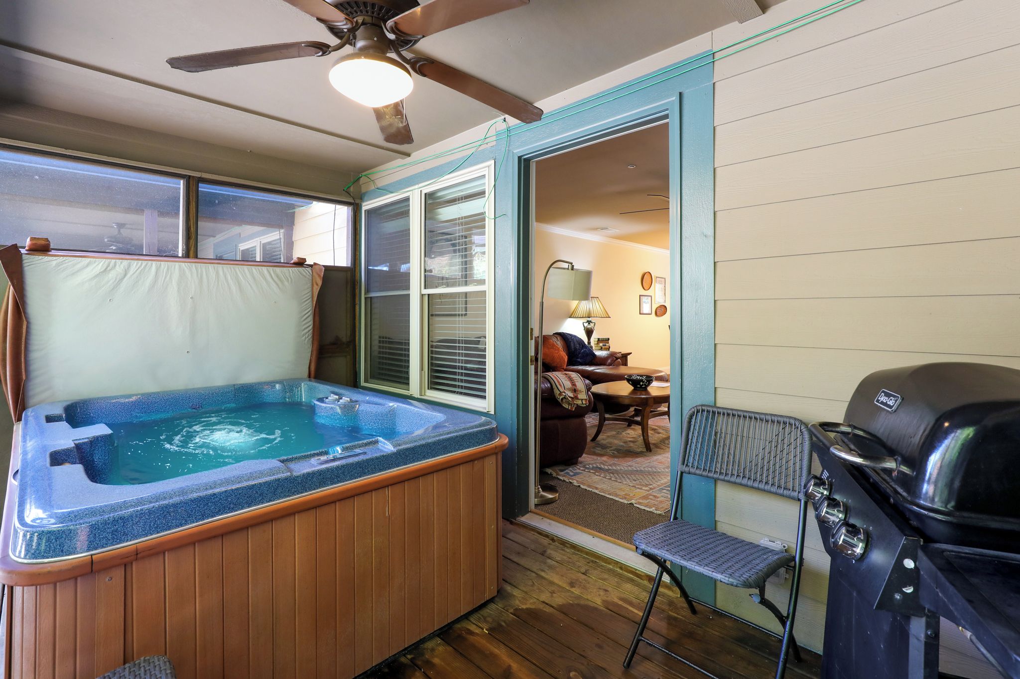 A hot tub in a room with a ceiling fan, a grill, and a dining area with a table and chairs.