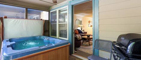 A hot tub in a room with a ceiling fan, a grill, and a dining area with a table and chairs.