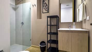 Un baño moderno con cabina de ducha de vidrio, tocador de madera, estante negro y una toalla colgada en la pared.